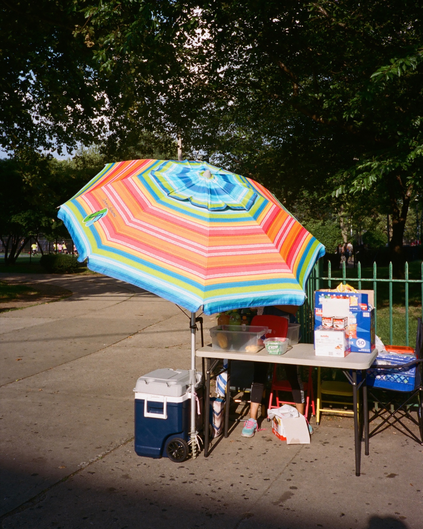 A striped umbrella shades a neighborhood snack vendor beside the soccer fields at Riverbank Park.