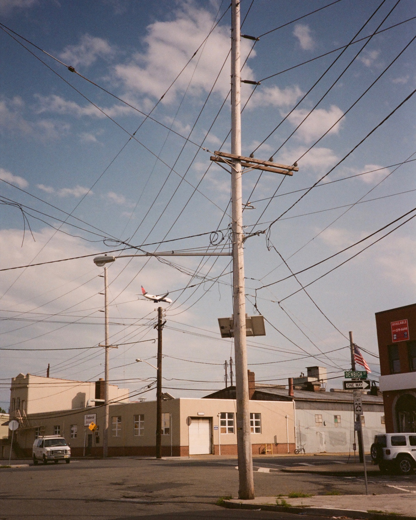 A jet on approach to Newark Liberty threads a web of utility wires above Denbigh Street.